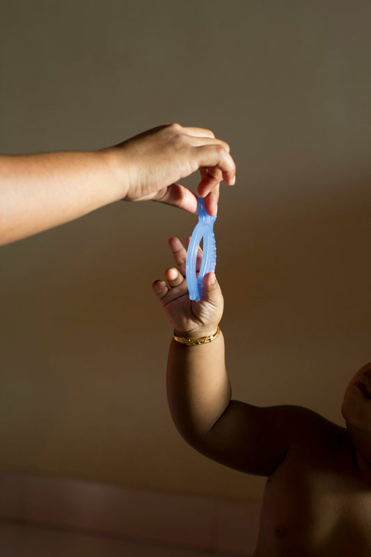 Adult hand holding a silicone teether toy up to a baby's hand