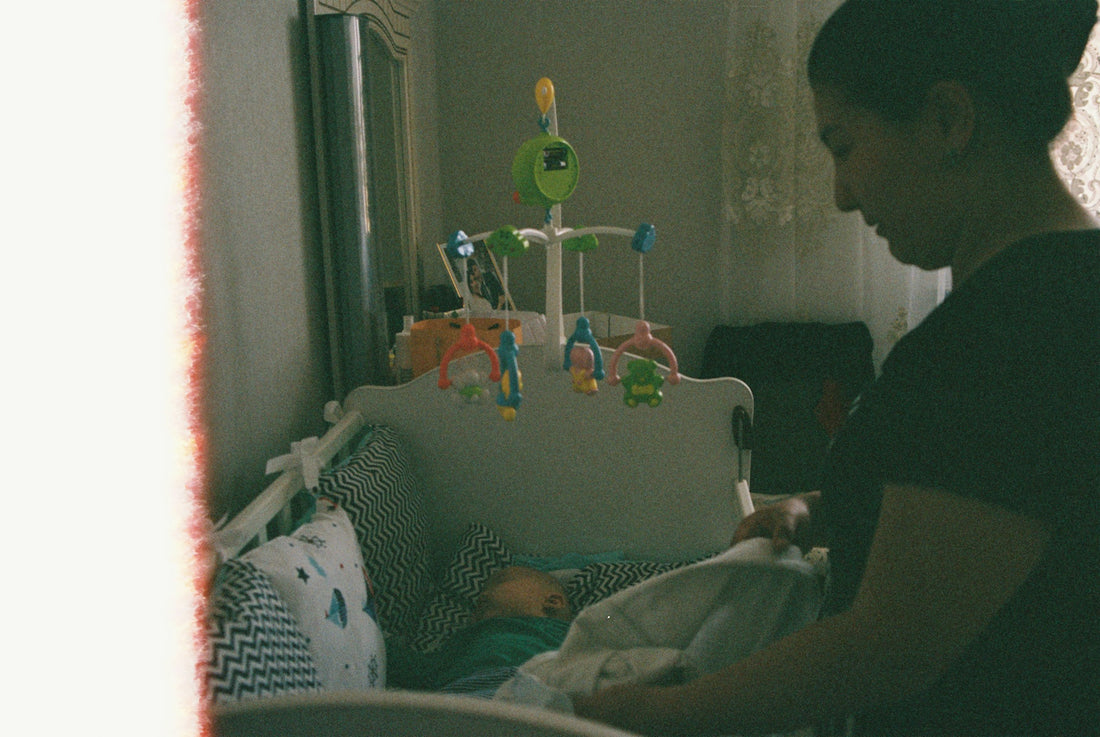 Parent tucking a sleeping baby into a crib in a nursery