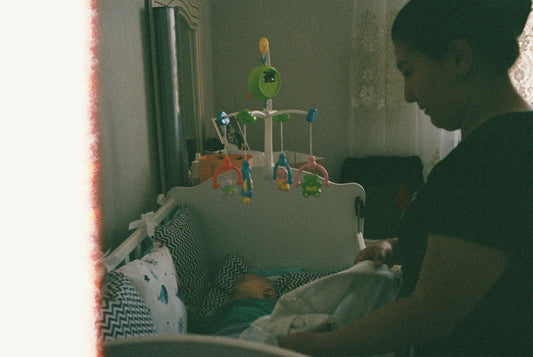 Parent tucking a sleeping baby into a crib in a nursery